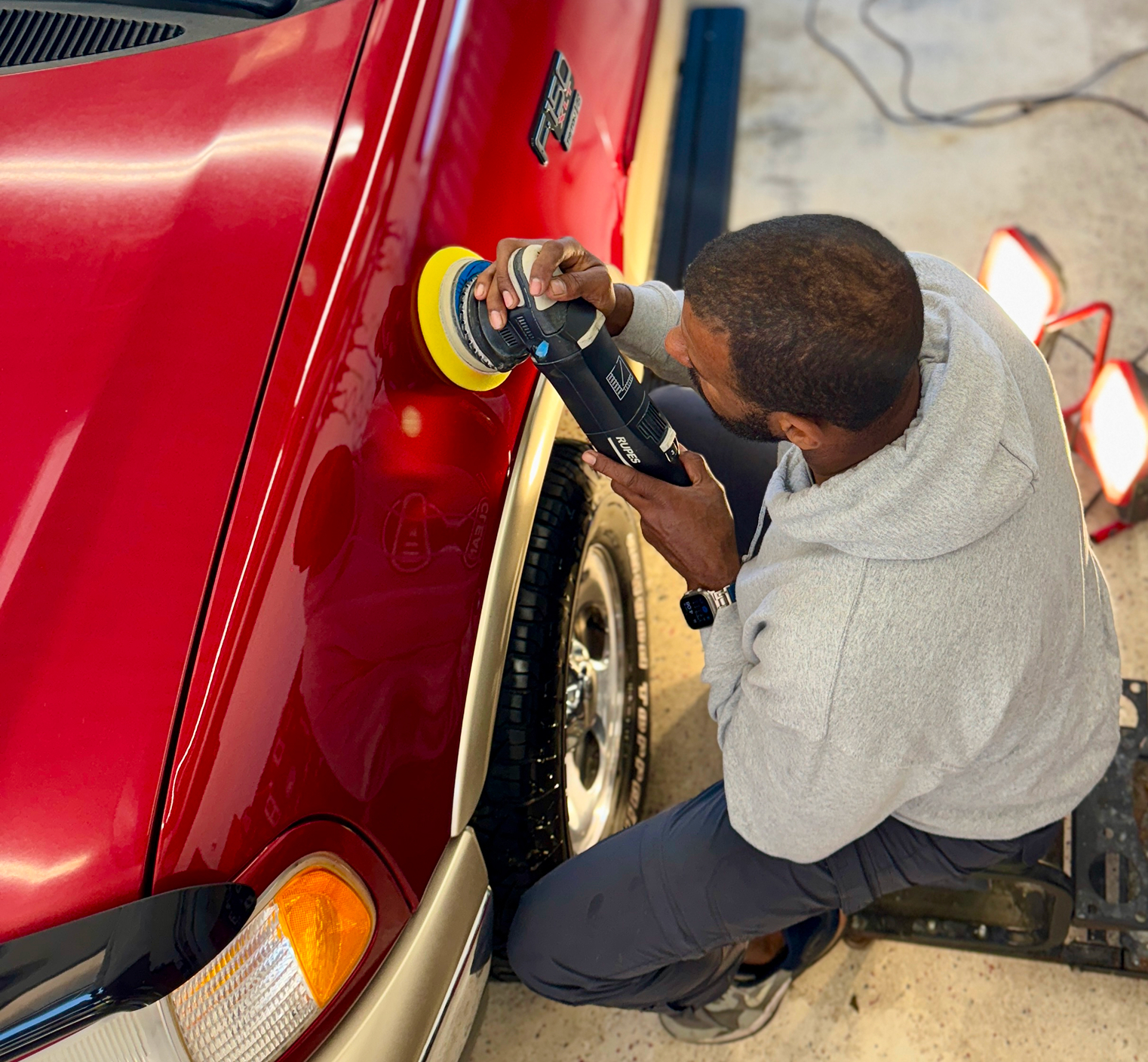 An employee of Clean Car Wash and Detail using a car polisher during paint correction services.